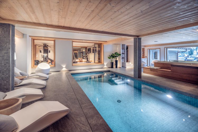 Indoor swimming pool at Chalet Harmony with modern loungers, adjoining gym and hot tub in a contemporary alpine spa area.