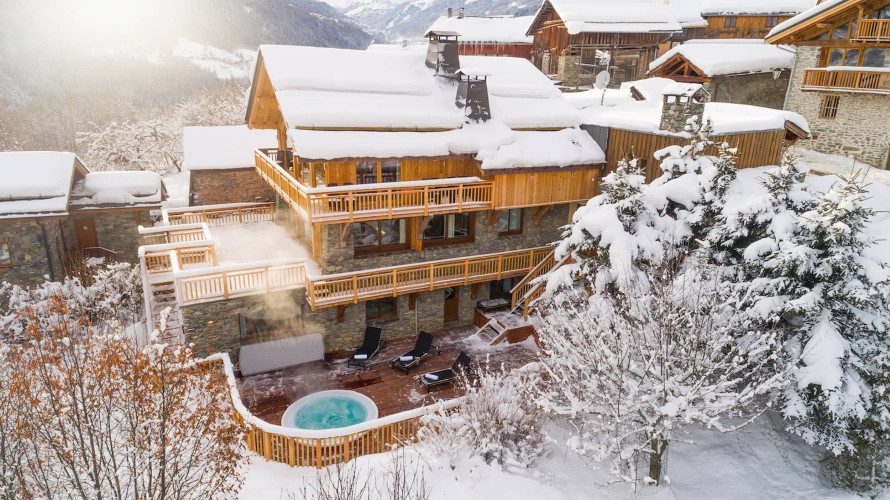 Aerial winter view of Chalet Iona with snow-covered roofs, wooden balconies, outdoor hot tub and surrounding alpine scenery.