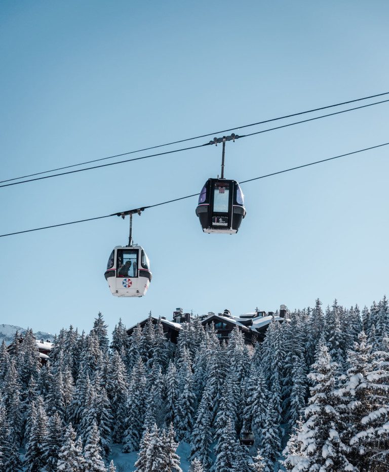 Gondola ski lifts travelling above snow-covered pine trees in Courchevel under a clear blue winter sky.