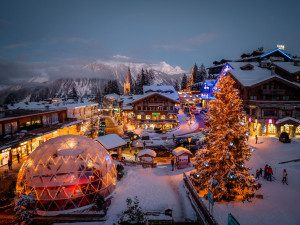 Courchevel 1850 village centre at dusk with snow-covered chalets, festive Christmas lights, a large illuminated tree and mountain views.