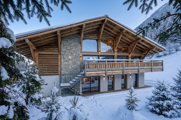 Close-up winter exterior of Chalet Patagonia with timber and stone architecture, large windows, balcony and deep surrounding snow.