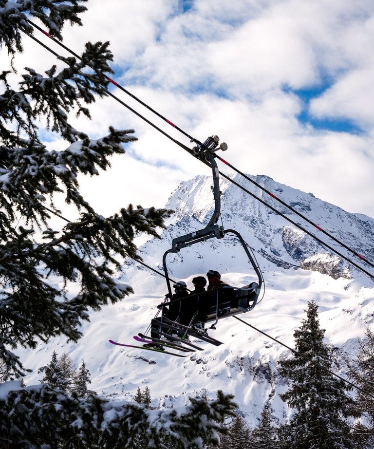 Chairlift carrying skiers through snowy trees in Sainte Foy Tarentaise with a dramatic mountain backdrop.