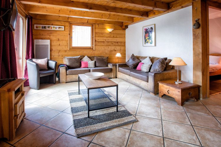 Lounge at Apartment Genepi with two leather sofas, armchair, wooden coffee table and warm timber-panelled walls.