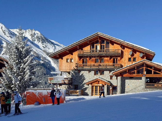Exterior of Apartment Le Clou beside the snowy ski piste, with traditional timber balconies and mountain views.