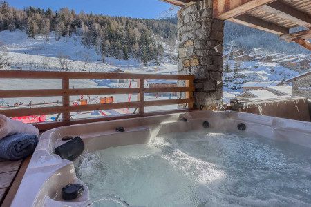 Hot tub on the terrace at Chalet La Vanoise overlooking the snowy ski piste, alpine chalets and surrounding mountains.