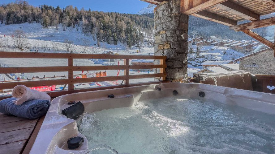 Hot tub on the terrace at Chalet La Vanoise overlooking the snowy ski piste, alpine chalets and surrounding mountains.
