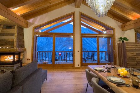 Open-plan lounge and dining area at Chalet Maison d'Etre with a fireplace, large picture windows and snowy mountain views.