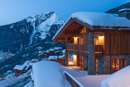 Exterior of Chalet Margaux at night with warm chalet lights, snow-covered surroundings, and alpine mountain views.