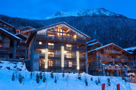 Chalet The Peak exterior at night with festive lights, snow-covered balconies and a dramatic mountain backdrop in Sainte Foy.