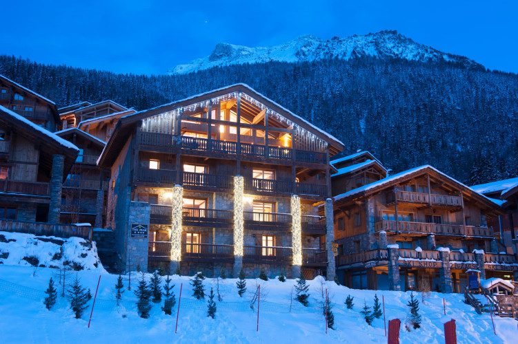 Chalet The Peak exterior at night with festive lights, snow-covered balconies and a dramatic mountain backdrop in Sainte Foy.