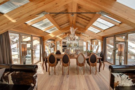 Opulent dining room at Chalet Backstage with a long wooden table, statement chandelier, vaulted timber ceiling and skylights.