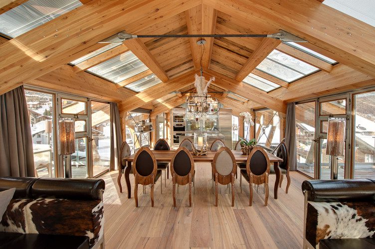 Opulent dining room at Chalet Backstage with a long wooden table, statement chandelier, vaulted timber ceiling and skylights.