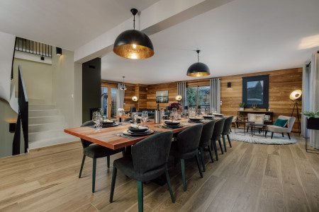 Second view of the dining area at Chalet La Bise with a large set table, dark upholstered chairs, pendant lighting and adjoining lounge.