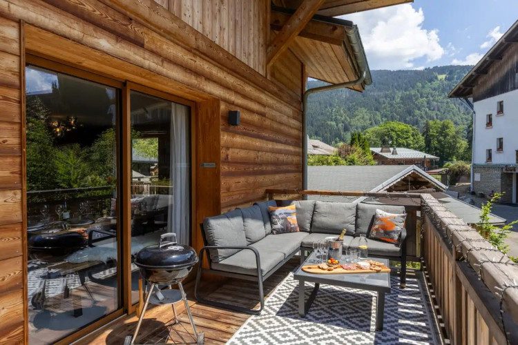 Sunny terrace at Chalet Le Faon with a barbecue, outdoor sofa, drinks and mountain views.
