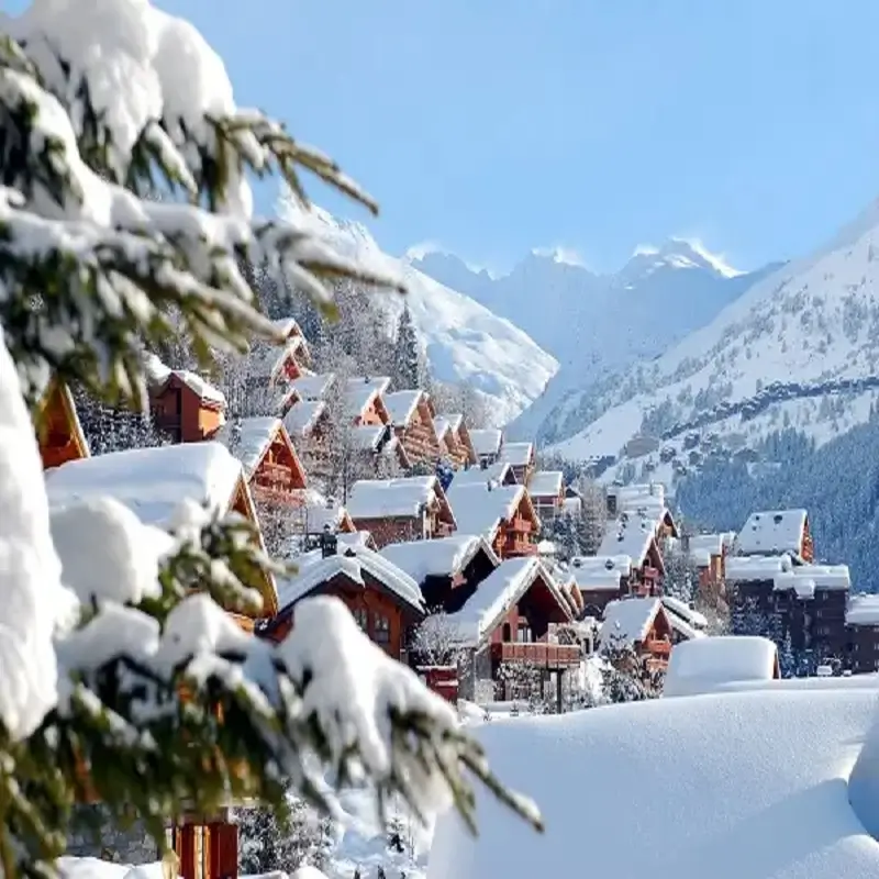 Snow-covered ski chalets in Méribel surrounded by pine trees and dramatic alpine mountain scenery.